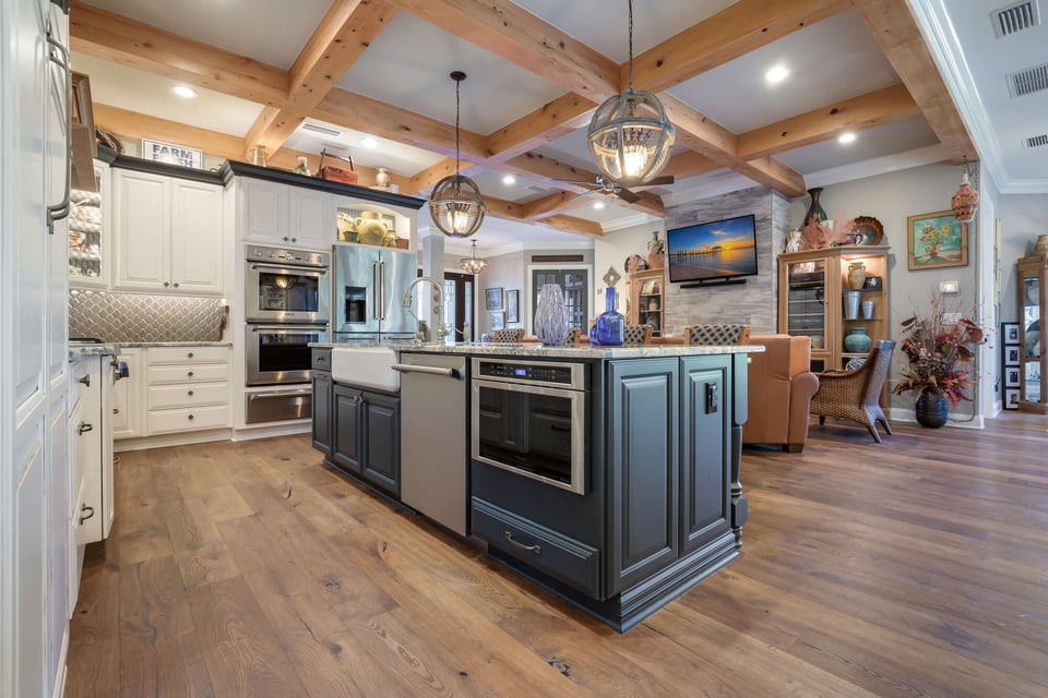 Open concept kitchen with large navy island and wood beam ceiling by BeeTree Homes in Jacksonville, FL