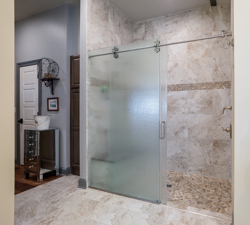 Bathroom remodel with pebble tile flooring and sliding shower door by BeeTree Homes in Neptune Beach, FL