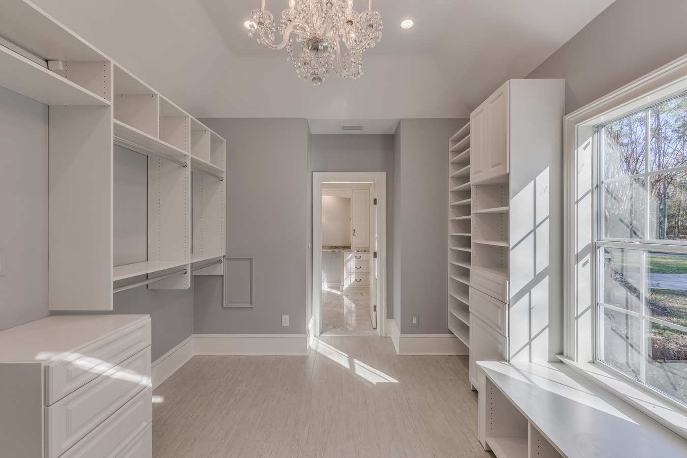 Walk-in closet with built-in shoe storage and chandelier lighting by BeeTree Homes in Jacksonville