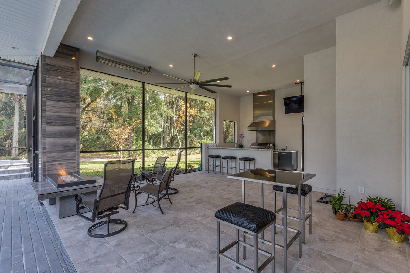 Screened outdoor living space with kitchen and fire feature by BeeTree Homes in Jacksonville, FL