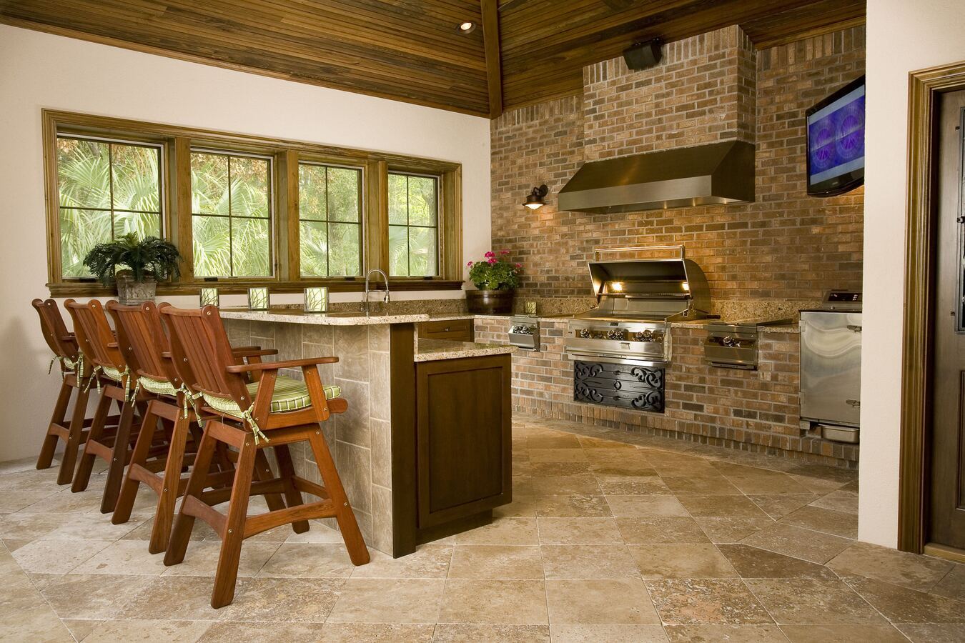 Brick-walled custom outdoor kitchen with bar seating in Jacksonville, FL by BeeTree Homes