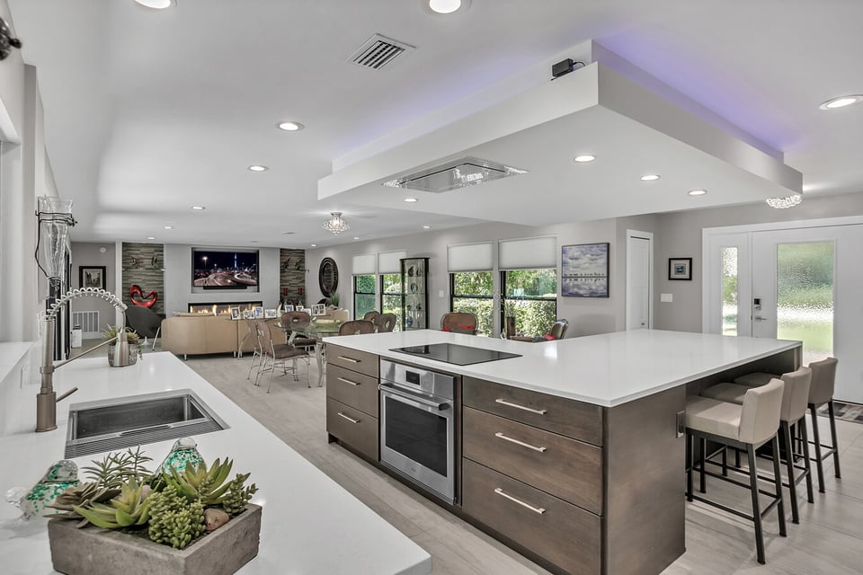 Open concept kitchen and living space with white countertops and wood accents by BeeTree Homes