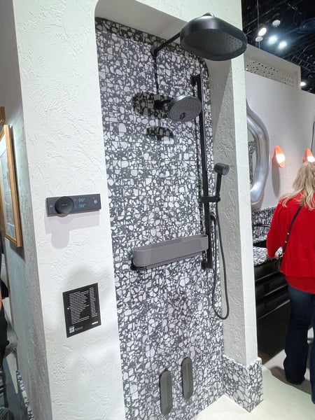 Matte black rainfall shower system with handheld sprayer and digital controls on patterned tile.