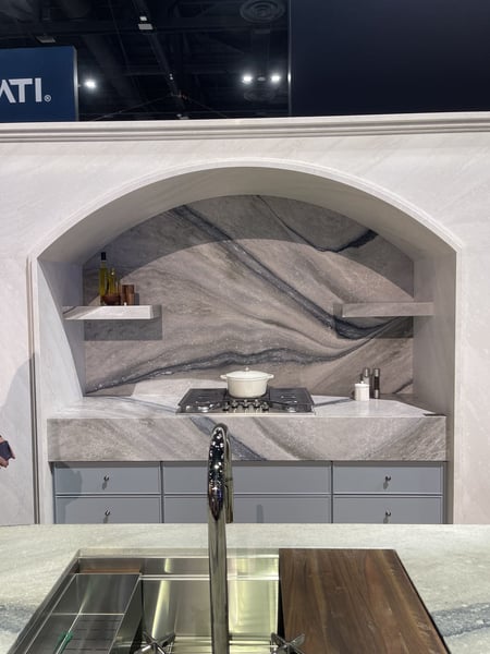 Modern gray kitchen display with stone backsplash, arched alcove, cooktop, sink, and wood cutting board.