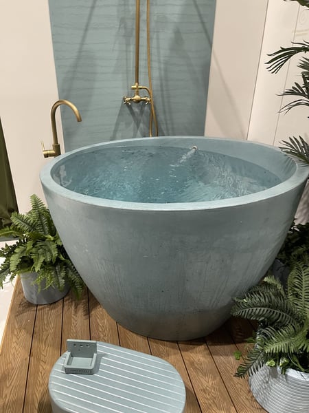 Round blue soaking tub with brass faucet and shower fixture, surrounded by decorative plants.