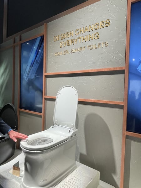 White Kohler smart toilet on display beneath a “Design Changes Everything” sign.