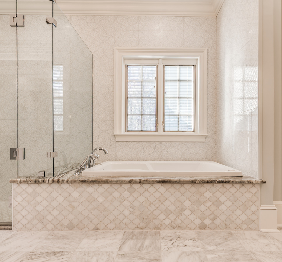 Elegant soaking tub next to frameless glass shower in custom bathroom by BeeTree Homes Jacksonville