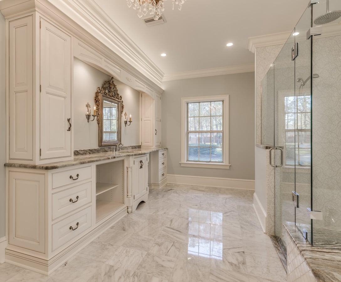 Grand custom bathroom with double vanity, marble floors, and glass shower by BeeTree Homes
