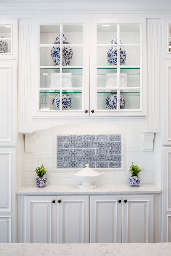 White custom kitchen display with glass-front cabinets and blue decorative vases by BeeTree